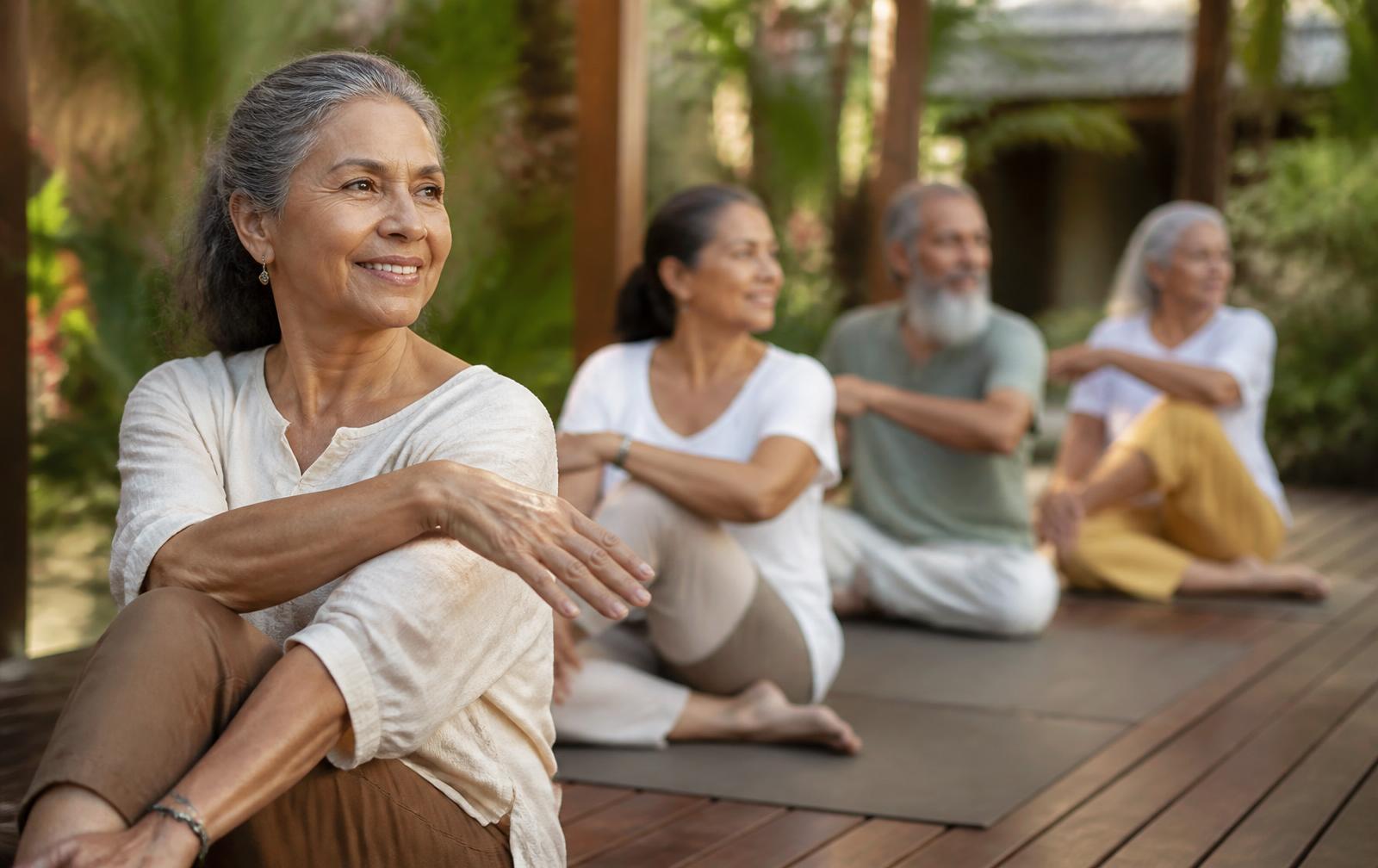Grupo de adultos mayores practicando yoga suave en el jardín de un hotel campestre